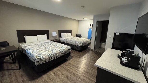 Quarto de hotel com duas camas, uma mesa, televisão e cozinha compacta.