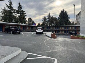 Ein Parkplatz mit einem weißen Auto, einem schwarzen Lastwagen und einem Gebäude mit vielen Fenstern und einer Ziegel-Fassade.