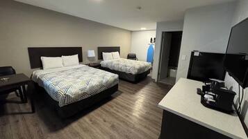 A hotel room with two beds, a desk, a TV, and a kitchenette.