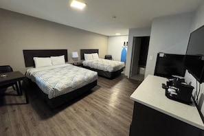 Ein Hotelzimmer mit zwei Betten, einem Schreibtisch, einem Fernseher und einer Küchenzeile.