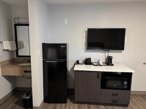 Eine kleine Küchenzeile mit Kühlschrank, Mikrowelle, Kaffeemaschine und einem Flachbildfernseher.