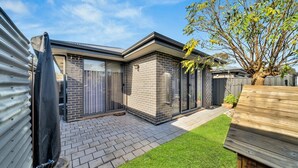 Une maison moderne avec une façade en briques, un patio couvert et une pelouse bien entretenue.