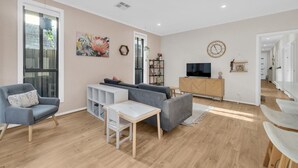 Un salon moderne avec un canapé gris, une table basse blanche et un téléviseur posé sur un meuble en bois.