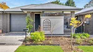 A modern two-story house with a brick facade, a garage door, and a well-maintained front yard with plants and a small tree. - The Barker Base | Gateway to the Hills (Mount Barker)