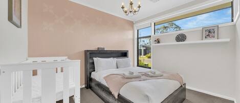 A bedroom with a bed, a crib, a chandelier, a window with a view, and a shelf with clocks.