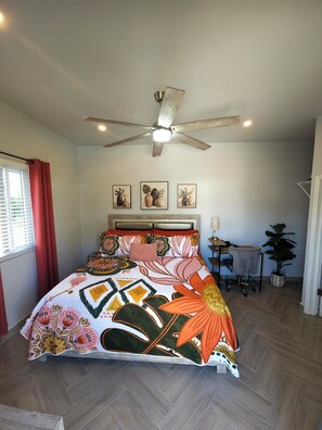 A bedroom with a bed, a ceiling fan, a desk, and a potted plant.