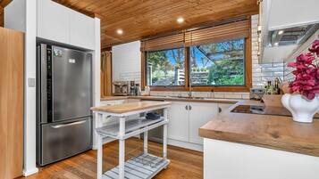 Een moderne keuken met een roestvrijstalen koelkast, houten kasten, een houten aanrecht en een raam met uitzicht op groen.
