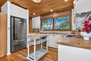 Una cocina moderna con un refrigerador de acero inoxidable, armarios de madera, encimera de madera y una ventana con vistas a zonas verdes.