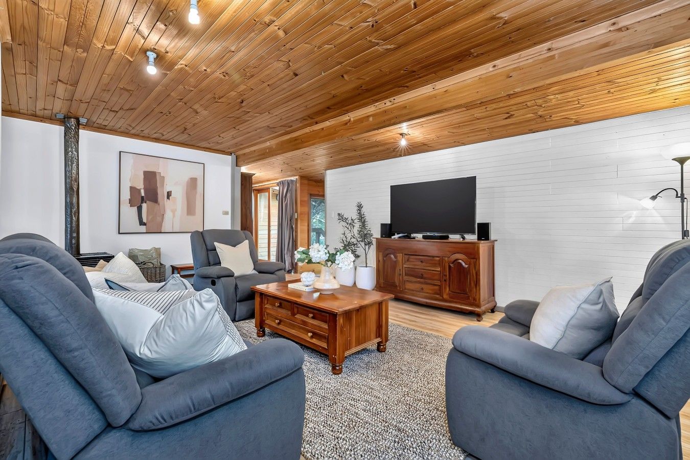 Un salon moderne avec un plafond en bois, un téléviseur à écran plat, des canapés gris et une table basse.