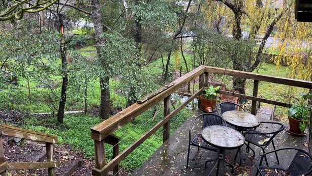 Una terraza de madera con mobiliario exterior, rodeada de abundante vegetación y árboles.