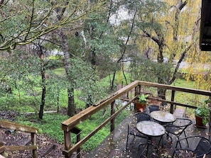Una terraza de madera con mobiliario exterior, rodeada de abundante vegetación y árboles.