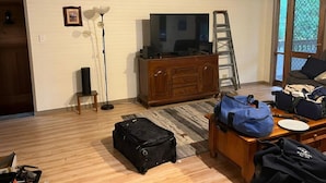 Una habitación con piso de madera, un armario de madera, una lámpara de pie, una escalera y un escritorio con bolsas.