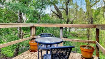 Une terrasse extérieure avec une rambarde en bois, une table ronde, deux chaises et deux plantes en pot.