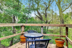 Une terrasse extérieure avec une rambarde en bois, une table ronde, deux chaises et deux plantes en pot.