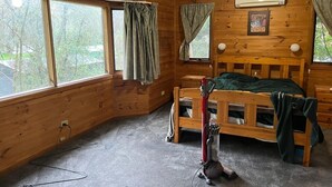 Una habitación de cabaña de madera con literas, un ventilador de techo y ventanas amplias.