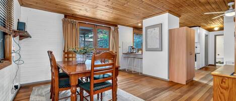 A dining area with a wooden table and chairs, a kitchen area with a counter and stools, and a ceiling with wooden beams.