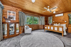 L’intérieur d’une cabane en bois, avec un lit, une chaise, un tapis rond et un ventilateur de plafond.