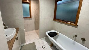 Un baño con una bañera blanca, un tocador de madera, un ventanal y piso de baldosas.