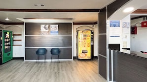 Een receptiegedeelte met een automaat, twee stoelen en een prikbord.