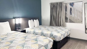 Een hotelkamer met twee bedden, een nachtkastje, een raam met gordijnen en een uitzicht op een trap.
