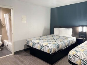 A hotel room with a bed, a nightstand, a wall-mounted light, and a bathroom visible through an open door. - Enjoy Affordable Comfort | 2 Units in Central Irving | Pet-Friendly Stay (Irving)