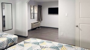 A room with two beds, a window with curtains, a mounted TV, and a radiator. - Enjoy Affordable Comfort | 2 Units in Central Irving | Pet-Friendly Stay (Irving)