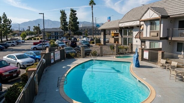 Una piscina con diseño curvo, rodeada por un estacionamiento con varios coches, y un edificio con techo plano y balcones.
