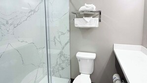 Un baño con cabina de ducha de vidrio, un inodoro blanco y un perchero para toallas.