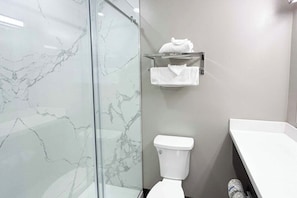 Een badkamer met een glazen douchecabine, een wit toilet en een handdoekrek.