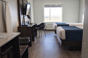 A hotel room with a desk, chair, two beds, a window with a view, and a mounted TV.