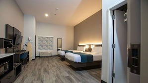 A hotel room with a bed, bedside table, lamp, and a desk with a chair.
