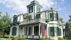 A large, white building with green trim and multiple windows, featuring a balcony and an American flag.