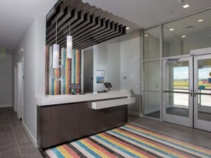 A reception area with a modern design, including a counter, a glass door entrance, and a striped rug.