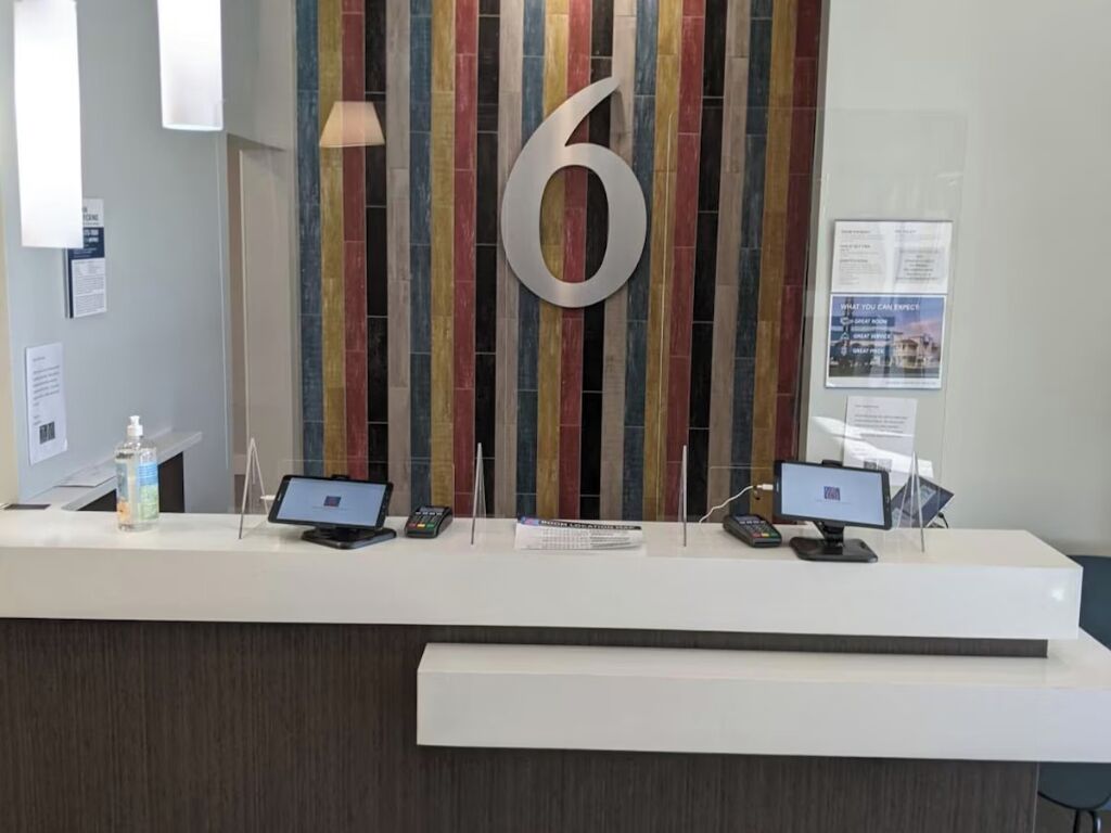 A reception desk with a large number '6' sign, a computer, a phone, and a bottle of hand sanitizer.