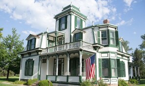 Un grande edificio bianco con decorazioni verdi e numerose finestre, dotato di un balcone e con una bandiera americana.
