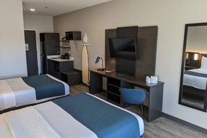 Camera d'albergo con due letti, una scrivania con sedia, televisione, specchio e angolo cottura.