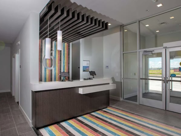 A reception area with a modern design, including a counter, a glass door entrance, and a striped rug.