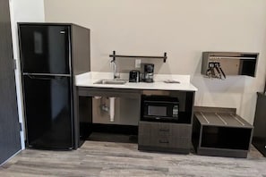 A compact kitchen with a black refrigerator, a sink, a coffee maker, and a microwave.