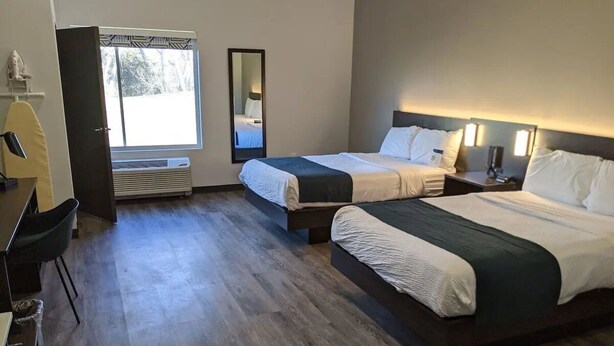 A hotel room with two beds, a desk, a chair, a mirror, and a window.
