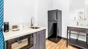 Una kitchenette compacta con microondas, cafetera, pileta y un refrigerador negro.