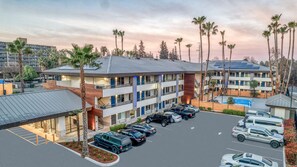 Ein mehrstöckiges Hotel mit Parkplatz, mehreren Autos und Palmen.