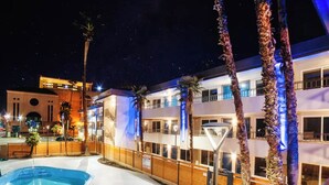 Un hotel con piscina, palmeras y un cielo nocturno.