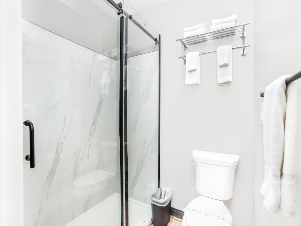 Et moderne badeværelse med en glasbrusekabine, et hvidt toilet og en håndklæderadiator.