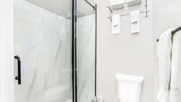 Et moderne badeværelse med en glasbrusekabine, et hvidt toilet og en håndklæderadiator.