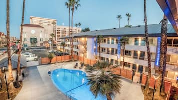 Un hotel con piscina, palmeras y vistas a un paisaje urbano.