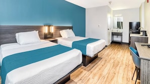 Ein Hotelzimmer mit zwei Betten, einem Schreibtisch, einem Sessel und einem Fernseher.