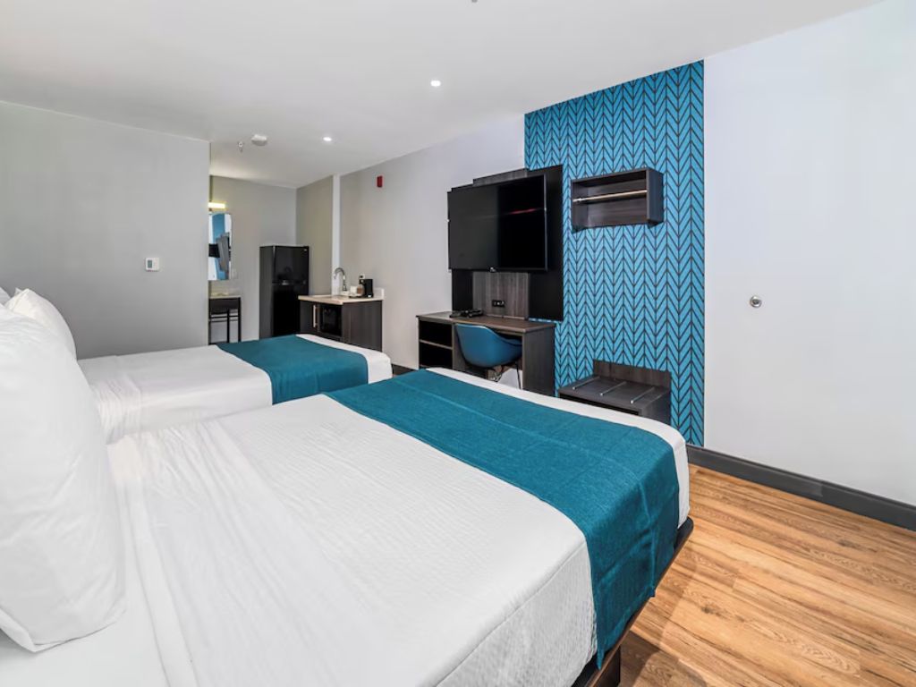 Habitación de hotel con dos camas, un escritorio con silla, televisión y kitchenette.
