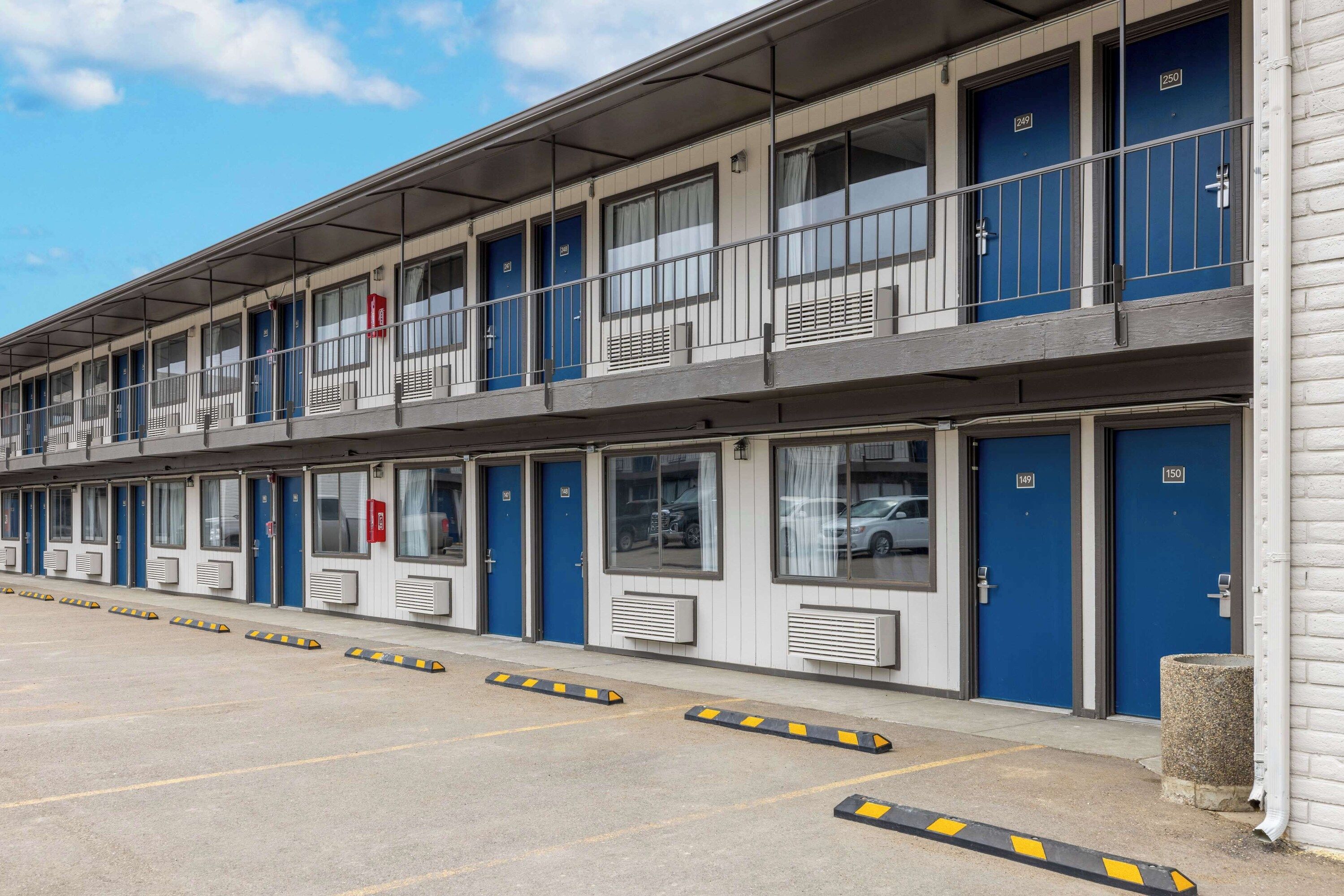 Un motel de varios pisos con puertas azules, habitaciones numeradas y un estacionamiento cubierto.