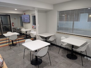 A modern dining area with white tables and chairs, a fire extinguisher, and a window with blinds. - 2 Welcoming Rooms w/ Kitchenette Near Rock Springs Historical Museum - 2.1 miles (Rock Springs)