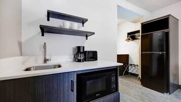 Una cocina moderna con un lavamanos, microondas, cafetera y armarios negros.